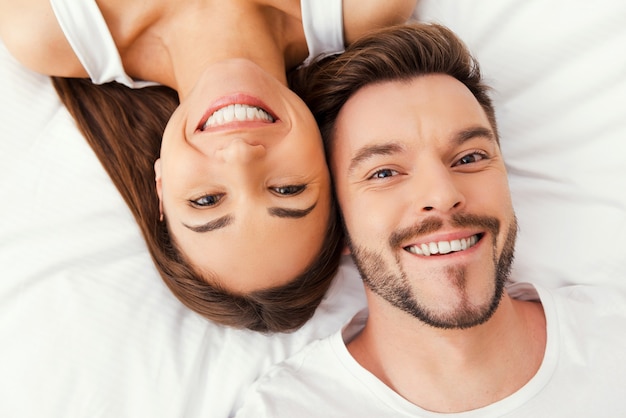 Enjoying their time together. Top view of beautiful young loving couple lying in bed together and smiling