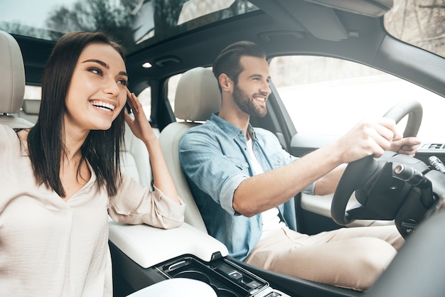 Enjoying travel. Beautiful young couple sitting on the front passenger seats and smiling while handsome man driving a car