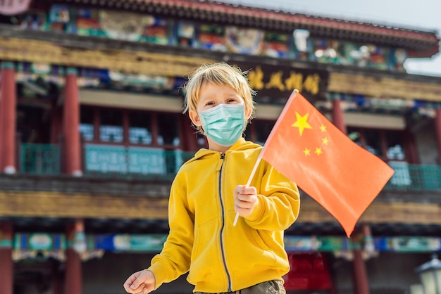 Enjoying vacation in china young boy in medical mask with national chinese flag on the background of