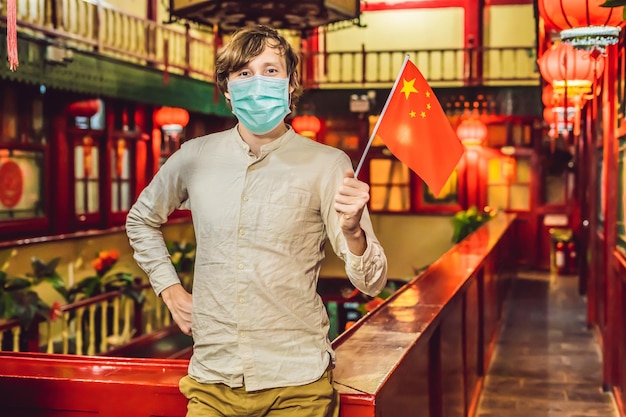 Enjoying vacation in china young man with a chinese flag in medical mask on a chinese background