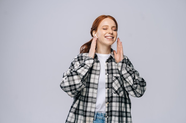 Enjoying young woman wearing wireless earphones dancing while listening popular song closed eyes