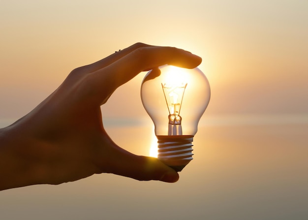 Enlightened Mind Hand Holding Glowing Light Bulb of Invention Delve into the world of bright ideas and ingenuity with this evocative image of a hand holding a glowing light bulb