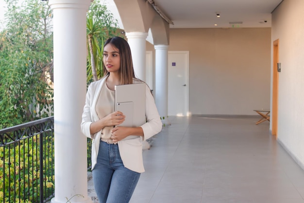 Enterprising girl carrying a tablet and laptop with her arms in a hotel