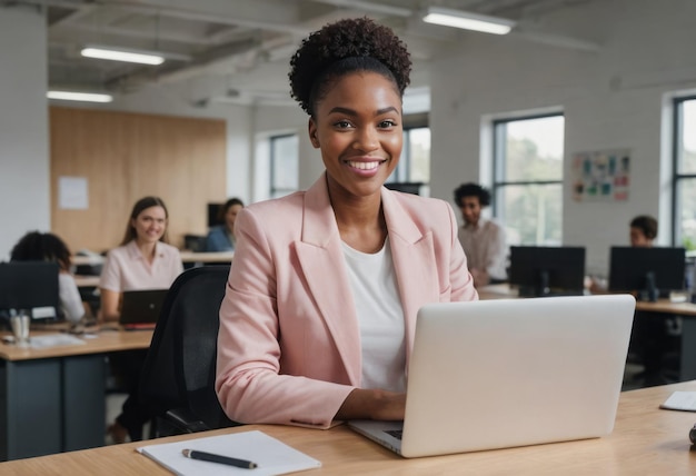 An enthusiastic businesswoman working on her laptop poised and smiling in a busy office her pink