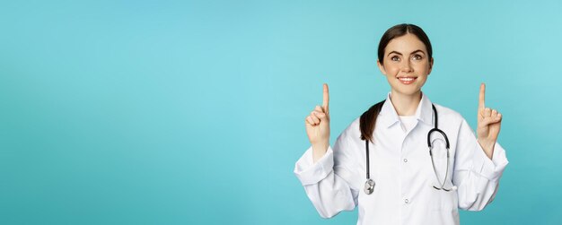 Photo enthusiastic medical worker young woman doctor in white coat stethoscope showing advertisement point