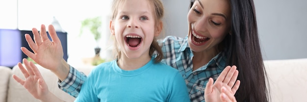 Enthusiastic mom and daughter with gift box are sitting on couch