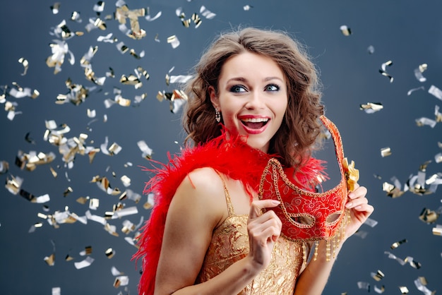 Enthusiastic woman holding a red carnival mask in her hands on a festive background with tinsel