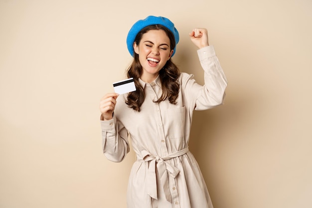 Enthusiastic young woman yearning to go shopping, dancing with credit card and celebrating, laughing and smiling