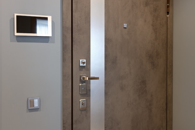 entrance door in a modern apartment hallway, video intercom device on the wall. Neutral tones.