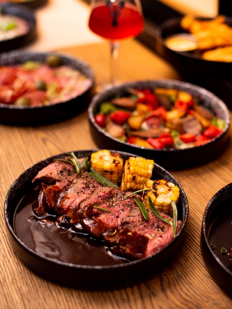 Entrecote Beef Grilled steak meat with fire flames on wooden cutting boardon with rosemary branch, pepper and salt. grilled vegetables, corn. Master chef cooking delicious grill barbecue.