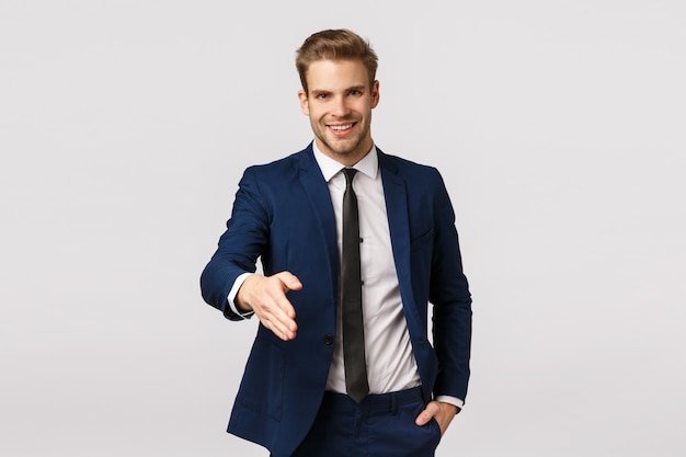 Entrepreneur, business and corporate concept. Attractive confident, smiling young blond businessman, extend arm for handshake say nice to meet you, greeting partners discuss income and deals