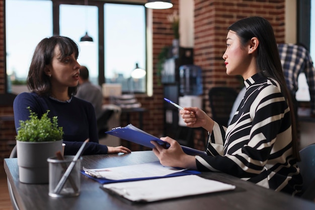 Entrepreneur person analyzing candidate cv resume asking recruitment question during interview meeting in startup company office. Asian manager recruiting woman for human resources job