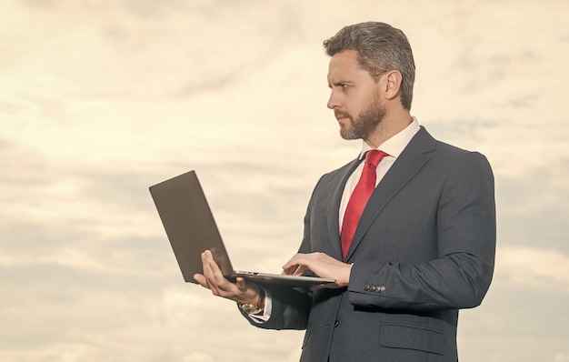 Entrepreneur in suit using laptop on sky background