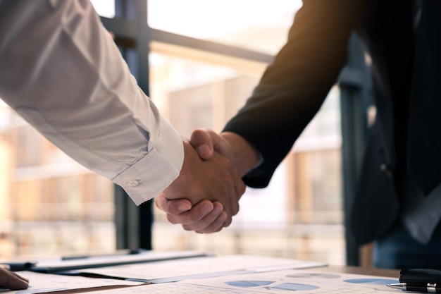 Entrepreneurs collaboration deal shaking hands in a modern office and financial paper graph on desk