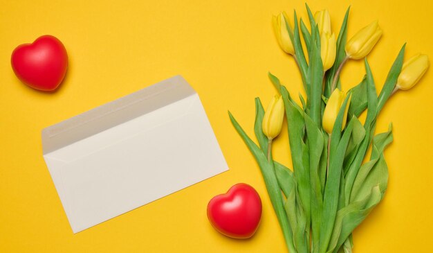 Envelope and red heart and bouquet of blooming tulips with green leaves on a yellow background