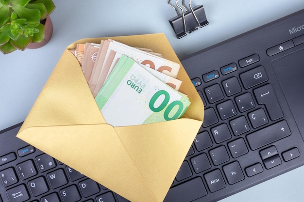 Envelope salaries under the table Golden envelope with cash euro banknotes on computer keyboard