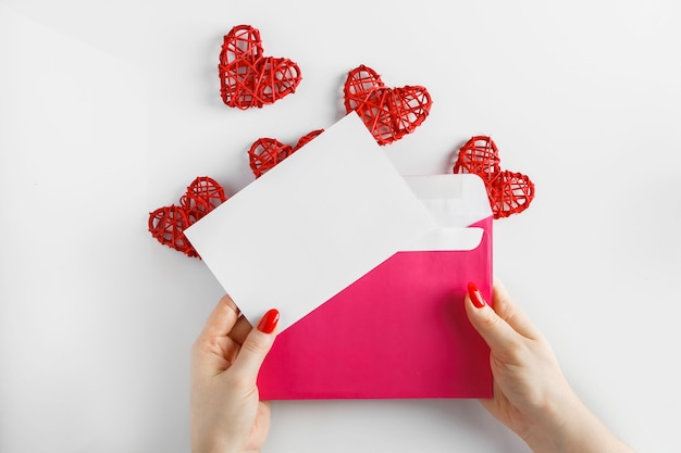 Envelope with a letter in hands on a white background. Pink envelope in hands and red heart