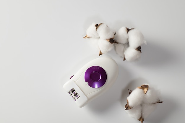 Epilator for hair removal and depilation, on a white background with cotton flowers, top view