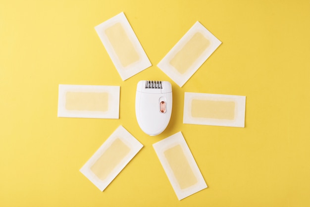 Epilator and wax strips on yellow background