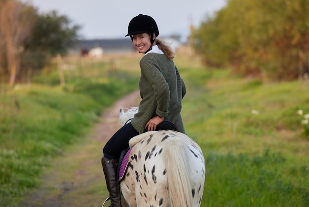 Photo equestrian horse and woman with portrait and smile in the countryside with ride on outdoor path happy ranch and animal with trainer rider and journey on a lawn with saddle helmet and fitness