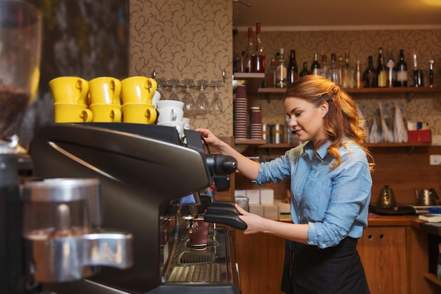 equipment, coffee shop, people and technology concept - barista woman making coffee by machine at cafe bar or restaurant kitchen