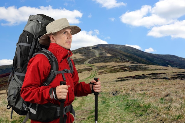 Equipped with traveler in a red jacket with Hiking poles looks into the distance