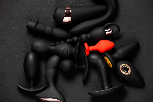 Erotic pleasure toys on a black background Sex gadgets and masturbation devices Pink dildo surrounded by black rubber and silicone sex toys anal butt plugs vibrators vaginal balls Top view