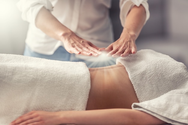 Esoteric healing by hands of a standing therapist, creating light above a young woman lying on her back.