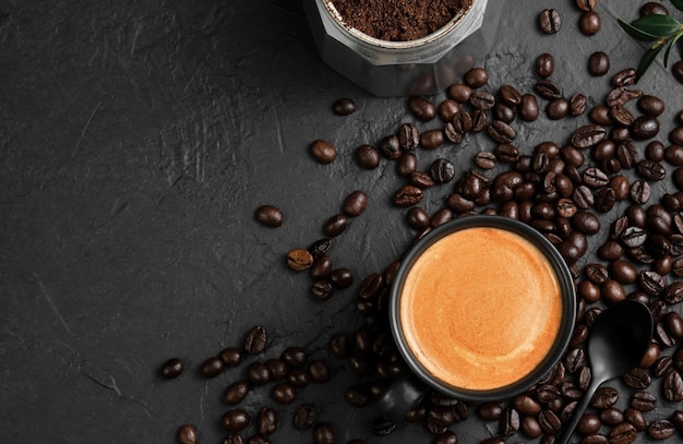 Espresso in a cup on a black table next to a coffee pot. Coffee beans and coffee ingredients on the table. Top view, place for text. Italian style breakfast idea.