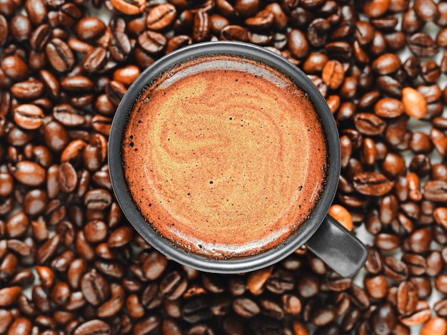 Espresso cup with froth among roasted coffee beans