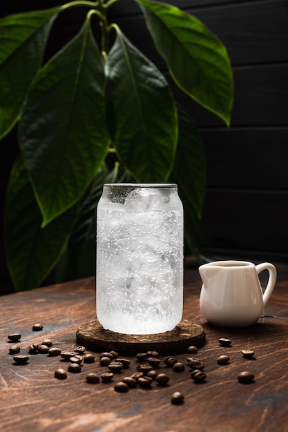 Espresso tonic in the making A highball glass filled with ice cubes tonic soda water coffee beans milk jug wooden background