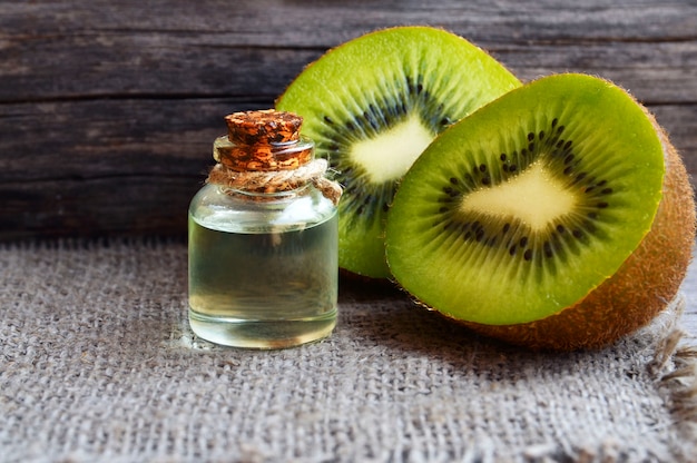 Essential kiwi seed oil in a glass jar with fresh halved kiwifruit on old wooden wall. .Aromatherapy,spa,beauty treatment and bodycare concept.Selective focus.