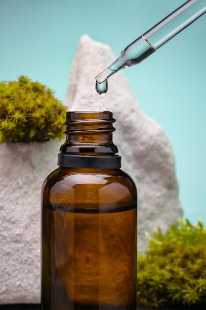 Essential oil in brown glass bottle among the moss and pipette with drop against green background