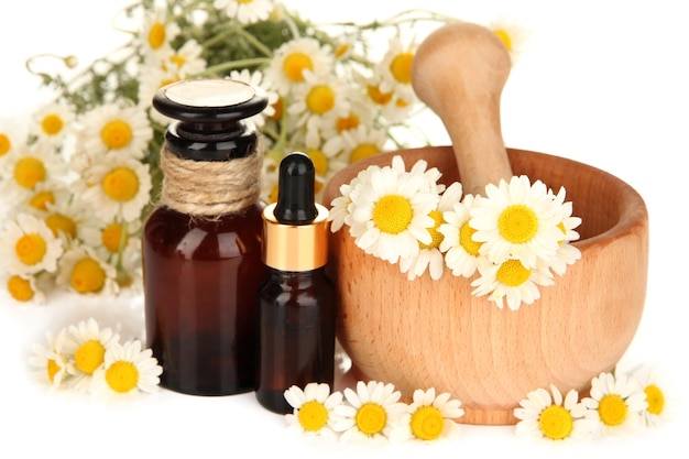 Essential oil and chamomile flowers in mortar close up