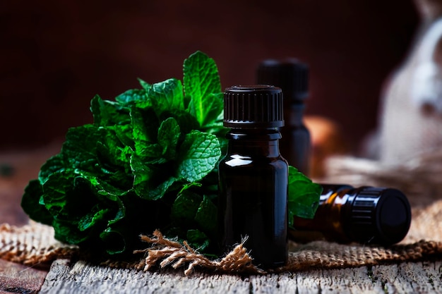 Essential oil of peppermint in a small brown bottle with fresh green mint rustic style vintage wooden background selective focus