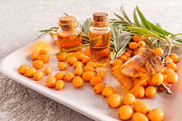 Essential oil of sea buckthorn in glass bottle with yellow berries on the branch with green leavesbeauty treatment Spa concept Selective focus