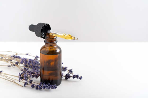 Essential oil with a dropper and lavender branches on a white background with copy space.