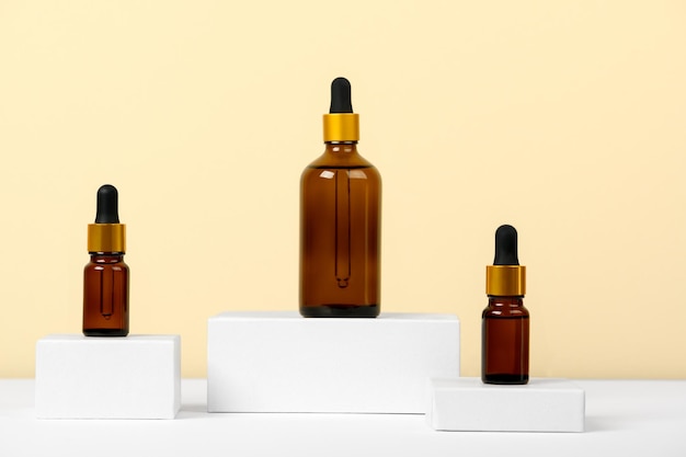 Essential oils on a beige background on white podiums, mockup. Cosmetic medical beauty product in brown glass bottles with a pipette for aromatherapy, alternative medicine. Natural aromatic remedy.