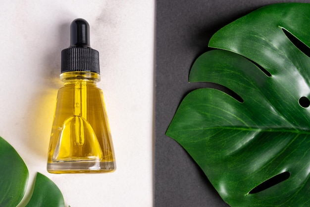 Essential oils with drops pipette and cream on marble background Grean monstera leaf decoration Professional bottle for facial and body treatment