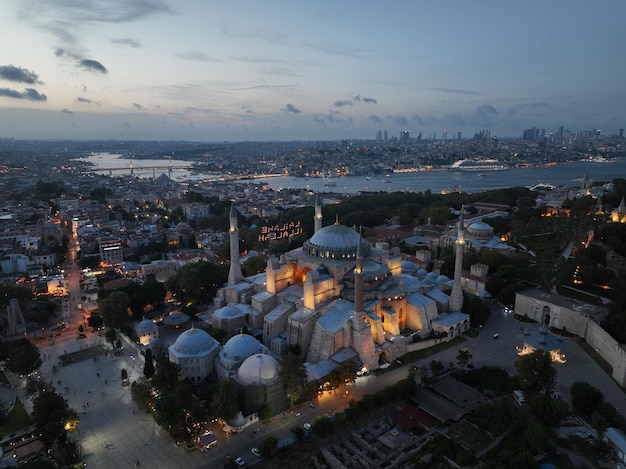 Establishing orbiting aerial drone shot of a Hagia Sophia Holy Grand Mosque with Bosphorus bridge and city skyline with a flag on the background in Fatih Istanbul Turkey at sunset