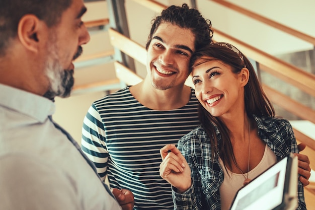 Estate agent is showing house to couple buyers, telling clients about home advantages. Interior designer is discussing renovation ideas with homeowners.