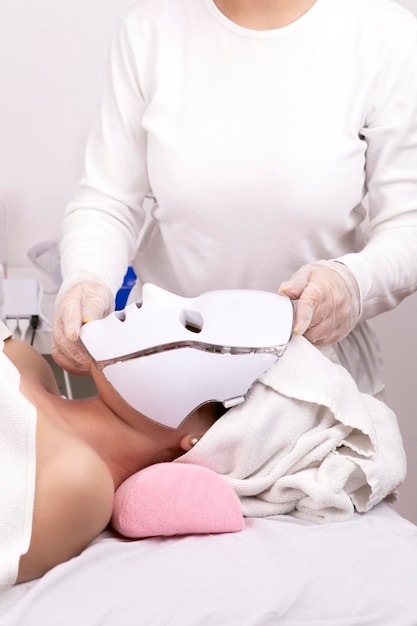 Esthetician preparing client for photodynamic facial mask therapy