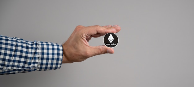 Ethereum coin in the man's hand on gray background. Crypto currency concept.