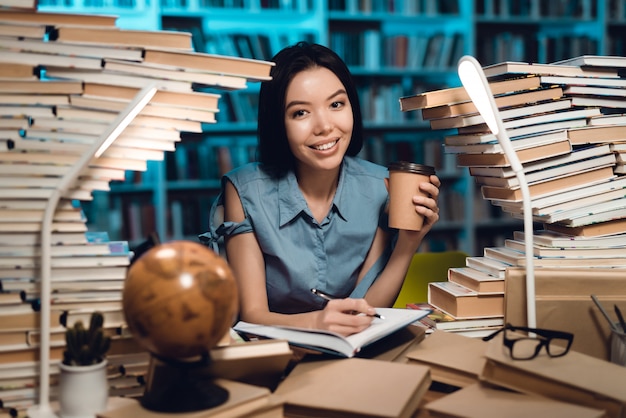 Ethnic asian girl surrounded by books in library. Student is writing in notebook.