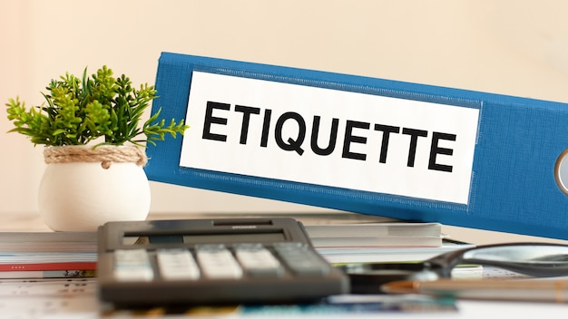 ETIQUETTE - blue binder on desk in the office with calculator, pen and green potted plant. Can be used for business, financial, education, audit and tax concept. Selective focus.