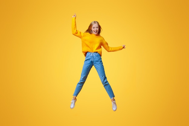 Photo euphoric teen girl jumping in air with hands up orange studio background with empty space