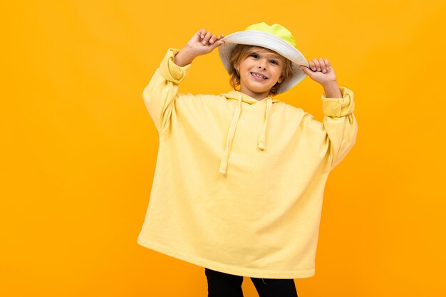 Photo european attractive boy with a panama in a light hoodie on a yellow wall