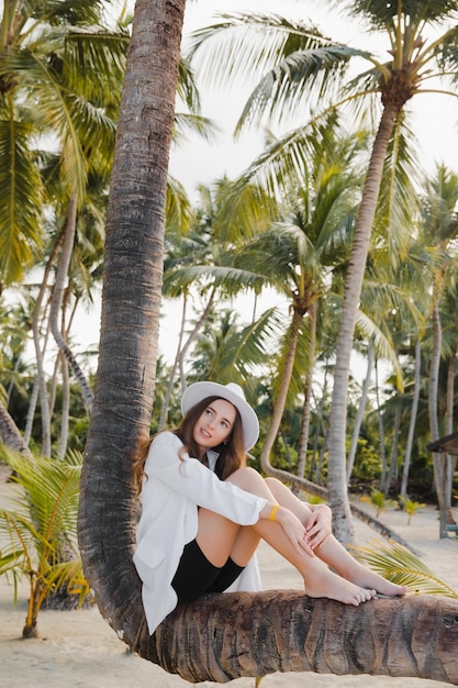 European beautiful happy dark haired girl near on coconut palm on the white sand beach