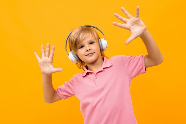 European blond boy in a pink T-shirt comes off to music in white headphones on orange