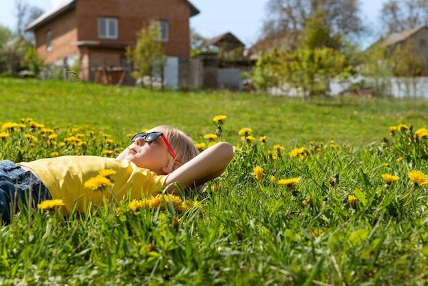 European boy lies on grass in dandelions flower filed looking to the sky on against house Outdoor portrait Side view